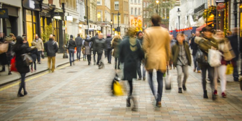 A busy high street scene with a couple holding hands and walking past fashion shops