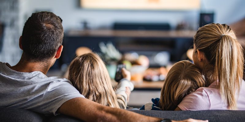 Back view of a relaxed family watching TV on sofa in the living room.